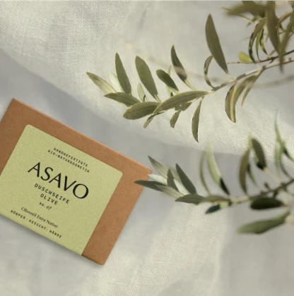 ASAVO Olivenölseife auf weißem Stoff mit Olivenzweigen zur Pflege der Hautbarriere.
