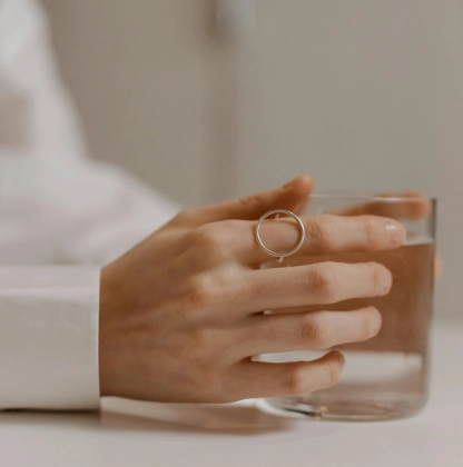 Nahaufnahme einer Hand, die ein Glas Wasser hält, um die Haut von innen mit Feuchtigkeit zu versorgen.